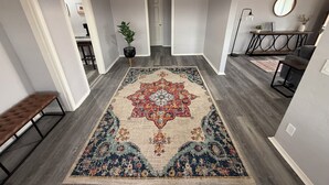 A hallway with a patterned rug, a bench, a potted plant, and a dining area with a table and chairs.
