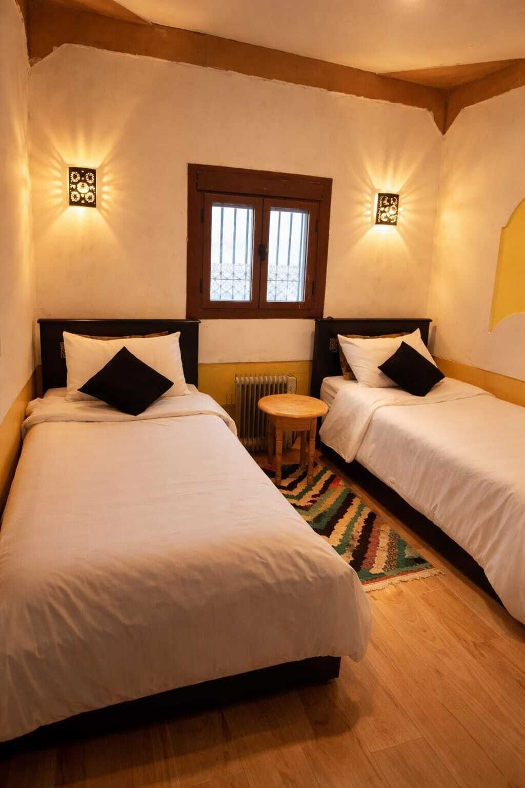A room with two beds, a small stool, a radiator, and a window with bars.