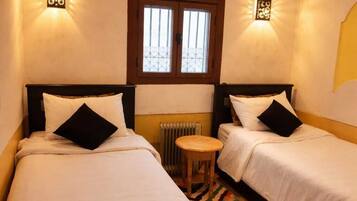 A room with two beds, a small stool, a radiator, and a window with bars.