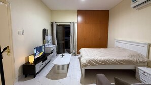 A hotel room with a bed, a desk, a chair, a wardrobe, and an air conditioning unit. - Perfect 1-bedroom villa with AC in charming Abu Dhabi (Abu Dhabi)