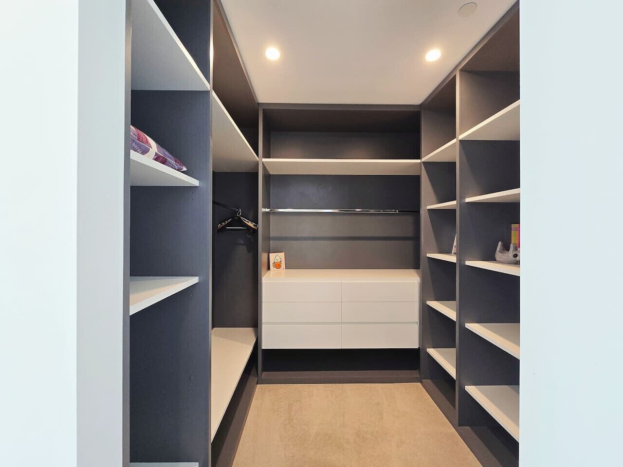 Ein begehbarer Kleiderschrank mit mehreren Regalen und Schubladen, einer Kleiderstange und einem hellen Teppich.