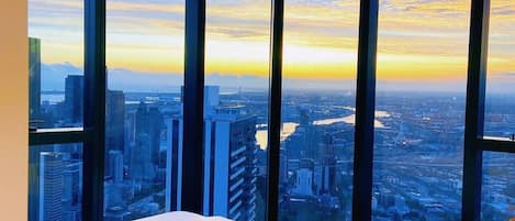 A bedroom with a large bed, a view of a cityscape at sunset, and a modern design.