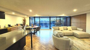 Ein modernes Wohnzimmer mit einer großen Eckcouch, einem Essbereich mit Tisch und Stühlen sowie einer Küchenzeile mit Arbeitsplatte und Geräten.