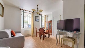 Un salon comprenant un canapé, un téléviseur posé sur un meuble, une table à manger avec des chaises et un lustre.
