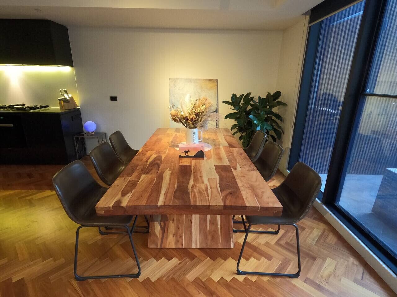 Un tavolo da conferenza con sedie, un vaso con fiori secchi e un quadro appeso al muro.
