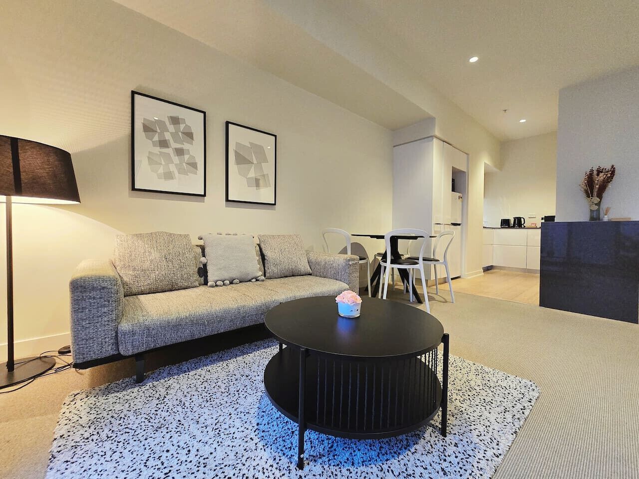 Ein modernes Wohnzimmer mit einer Couch, einem runden schwarzen Couchtisch und zwei gerahmten abstrakten Kunstwerken an der Wand.