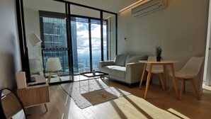 Un salon moderne doté d’une grande fenêtre, d’un canapé, d’une table basse et d’un coin repas avec des chaises.