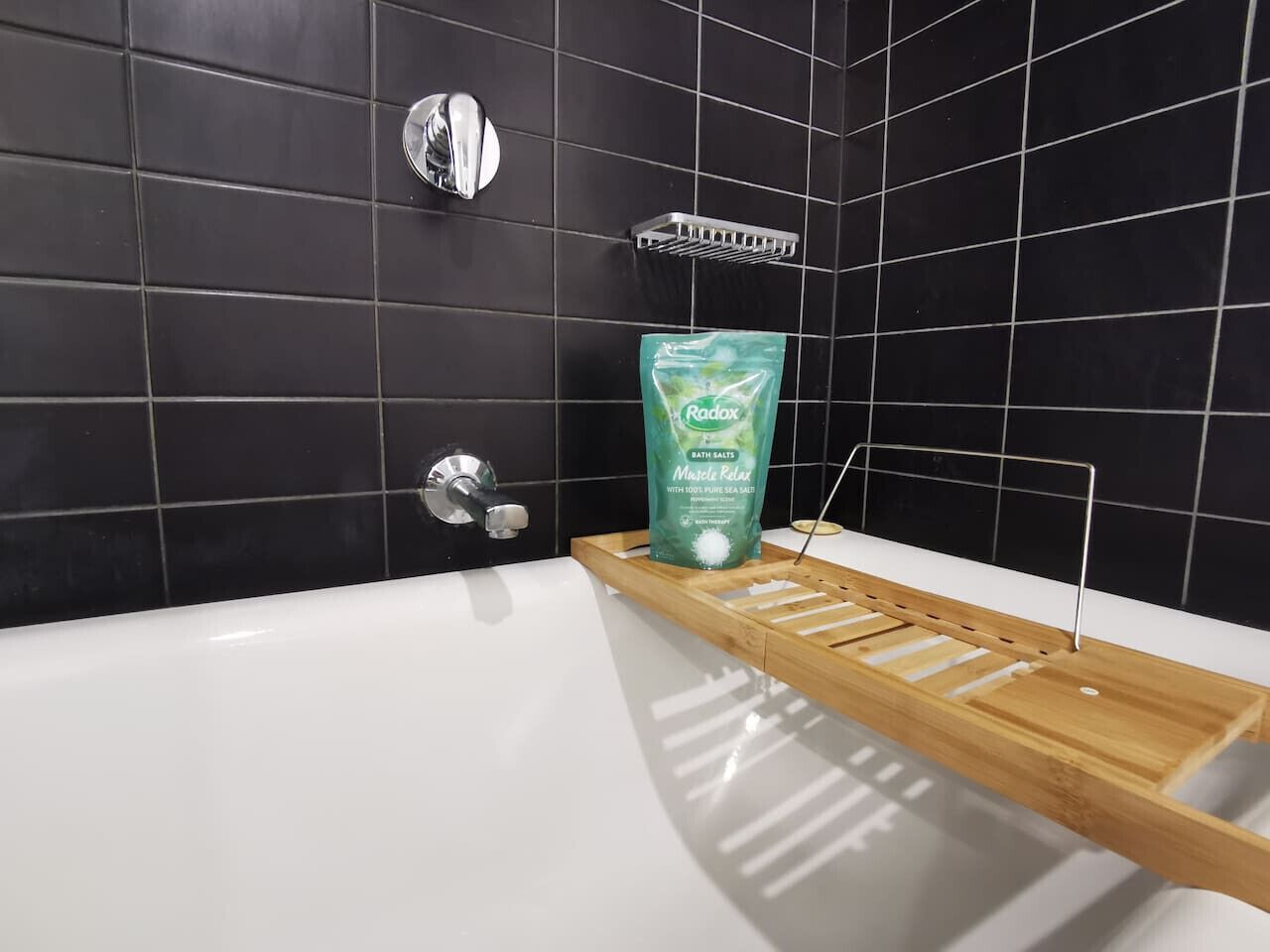 Een badkamer met een witte badkuip, een houten plank en een pak Radox badzout.