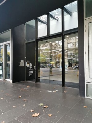 A modern building entrance with glass doors and windows, a tiled floor, and a reflection of a street scene. - MHYL #CBD 1BR| Southern Cross| Crown Casino| DFO (Melbourne)