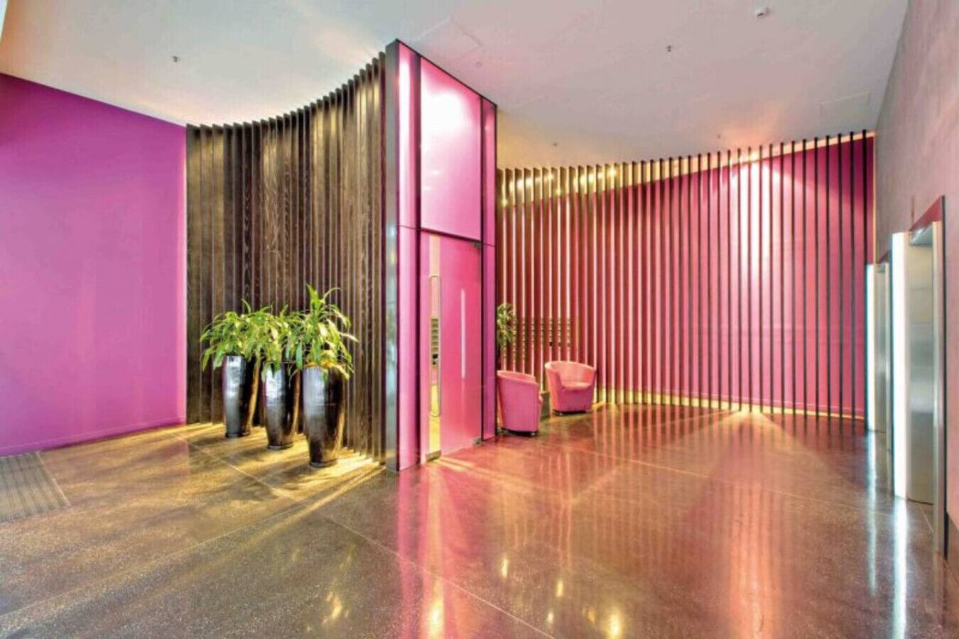 A modern lobby with a curved wall, a reception desk, and potted plants.