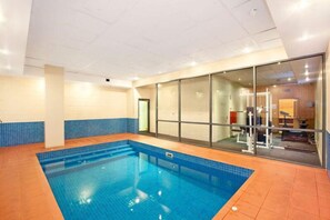 A large indoor swimming pool with clear blue water, surrounded by tiled walls and a glass partition. - MHYL #CBD 2BR| Southern Cross| Crown Casino| DFO (Melbourne)
