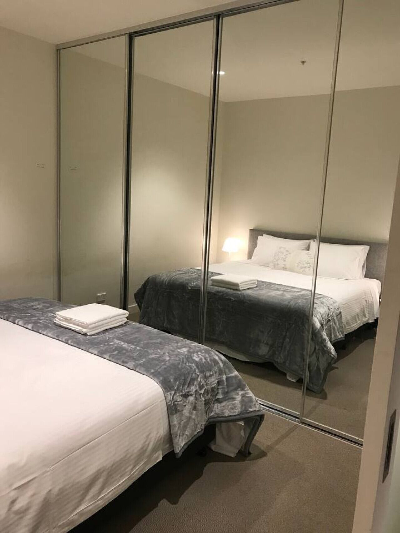 Ein Hotelzimmer mit zwei Betten, einem großen Spiegel und einem Nachttisch mit einer Lampe.