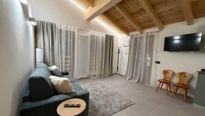 Un salon moderne avec un canapé, une petite table ronde, un téléviseur fixé au mur et des chaises en bois.