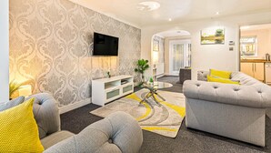 Ein modernes Wohnzimmer mit einem grauen Sofa, einem an der Wand montierten Fernseher und einem Essbereich mit Tisch und Stühlen.