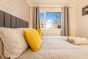 Een net opgemaakt bed met hoofdbord, twee kussens en dekbed.