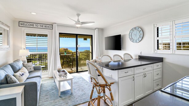 Een moderne woonkamer met een bank, salontafel en een rieten stoel. Door de schuifdeuren is een balkon met uitzicht op de oceaan zichtbaar.