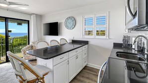 Een moderne keuken met een zwart aanrecht, witte kasten en een groot raam met zonwering.