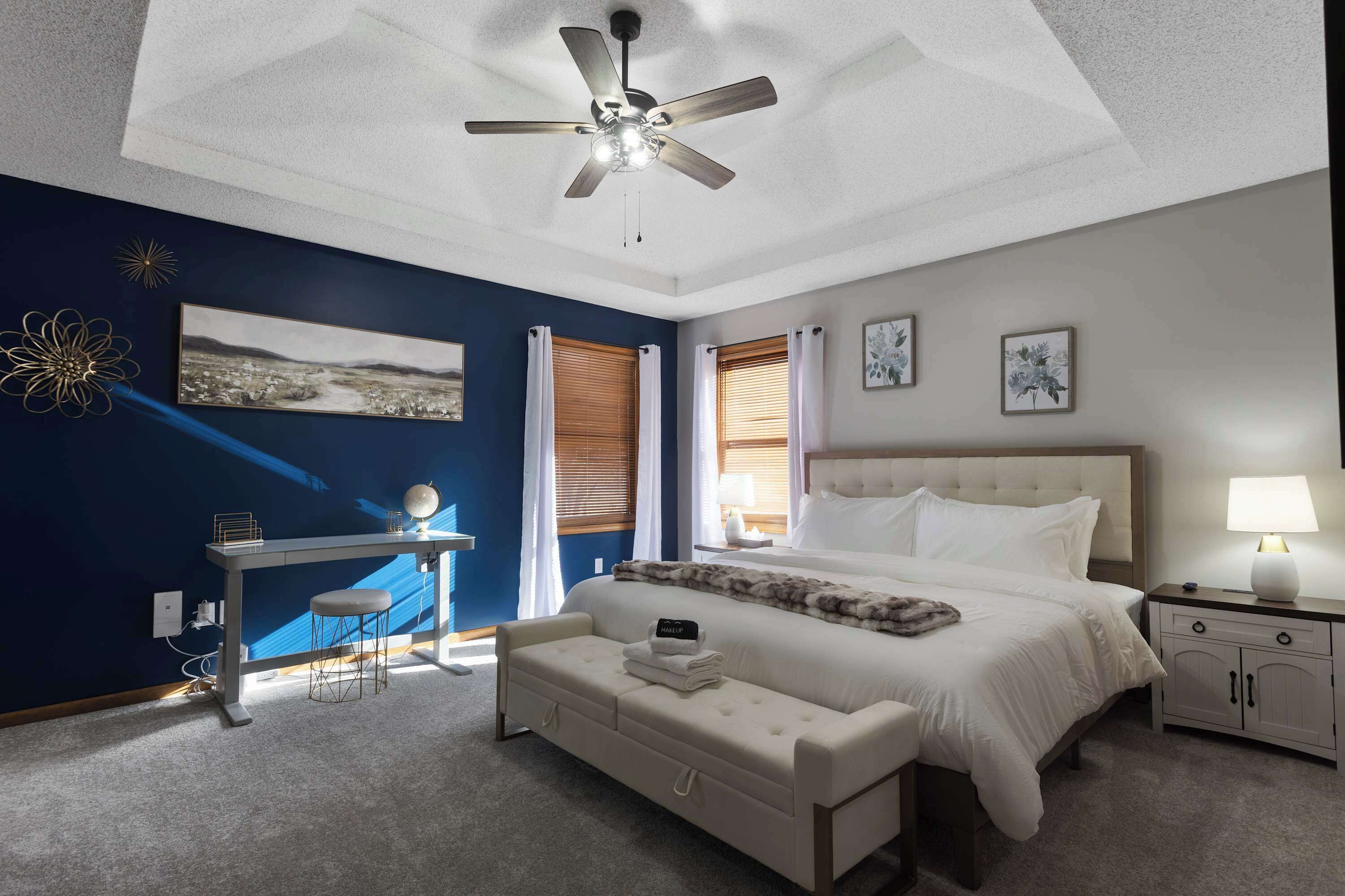 A modern bedroom with a large bed, a desk, and a ceiling fan.