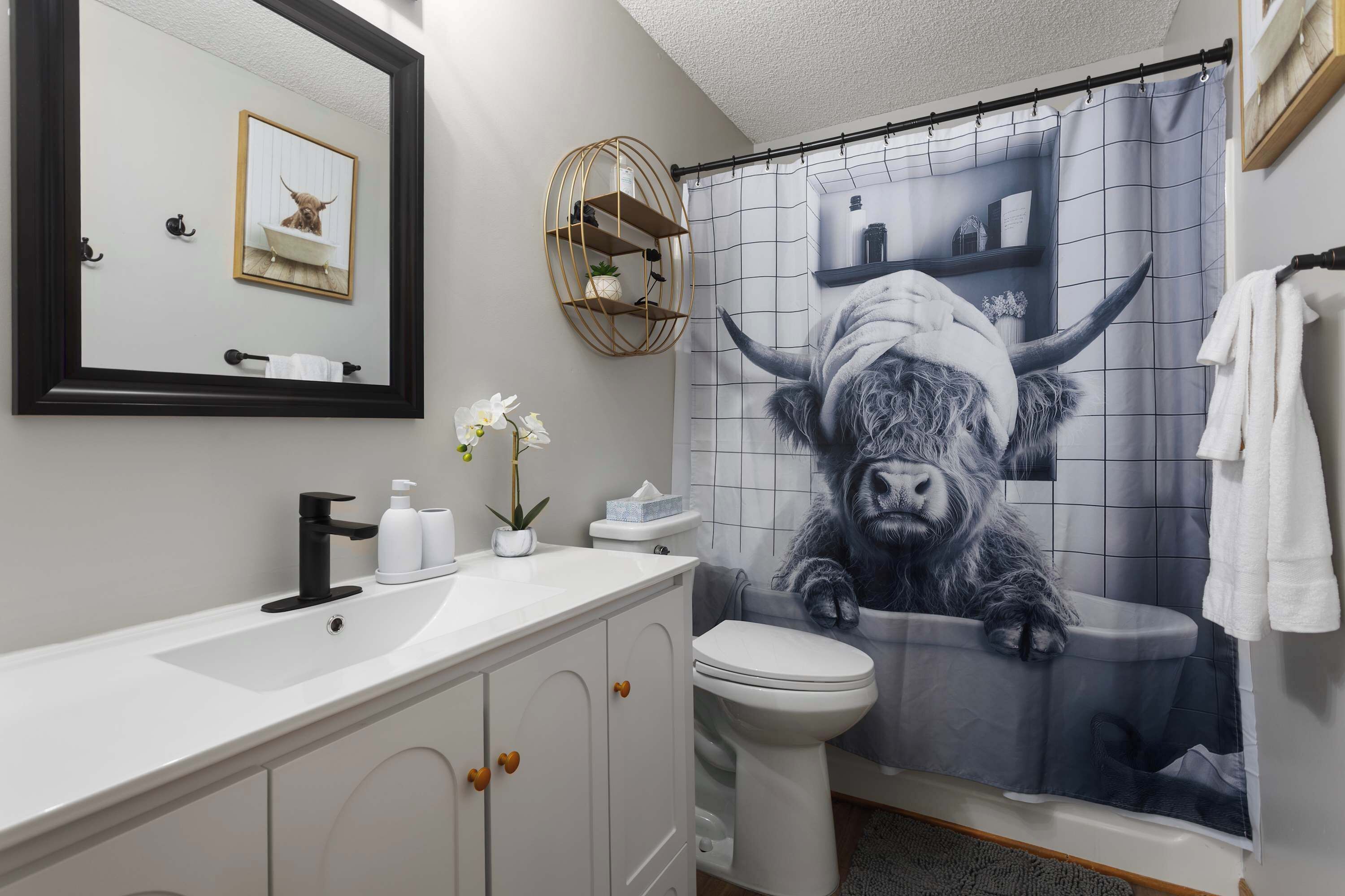 Une salle de bain avec un lavabo blanc, des toilettes, un miroir et un rideau de douche orné d’un motif de taureau.