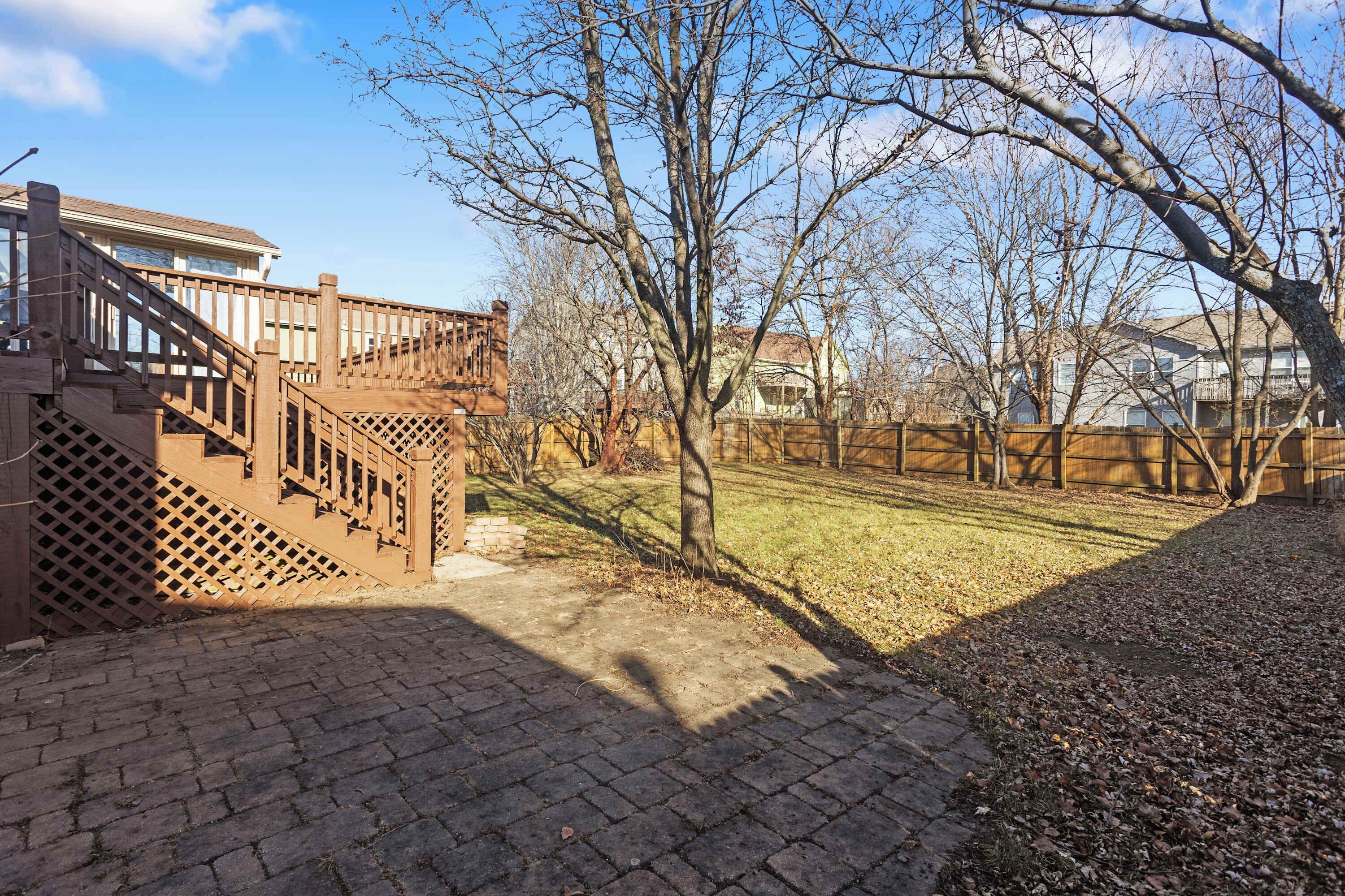 A backyard with a wooden deck, a brick pathway, and a grassy lawn.