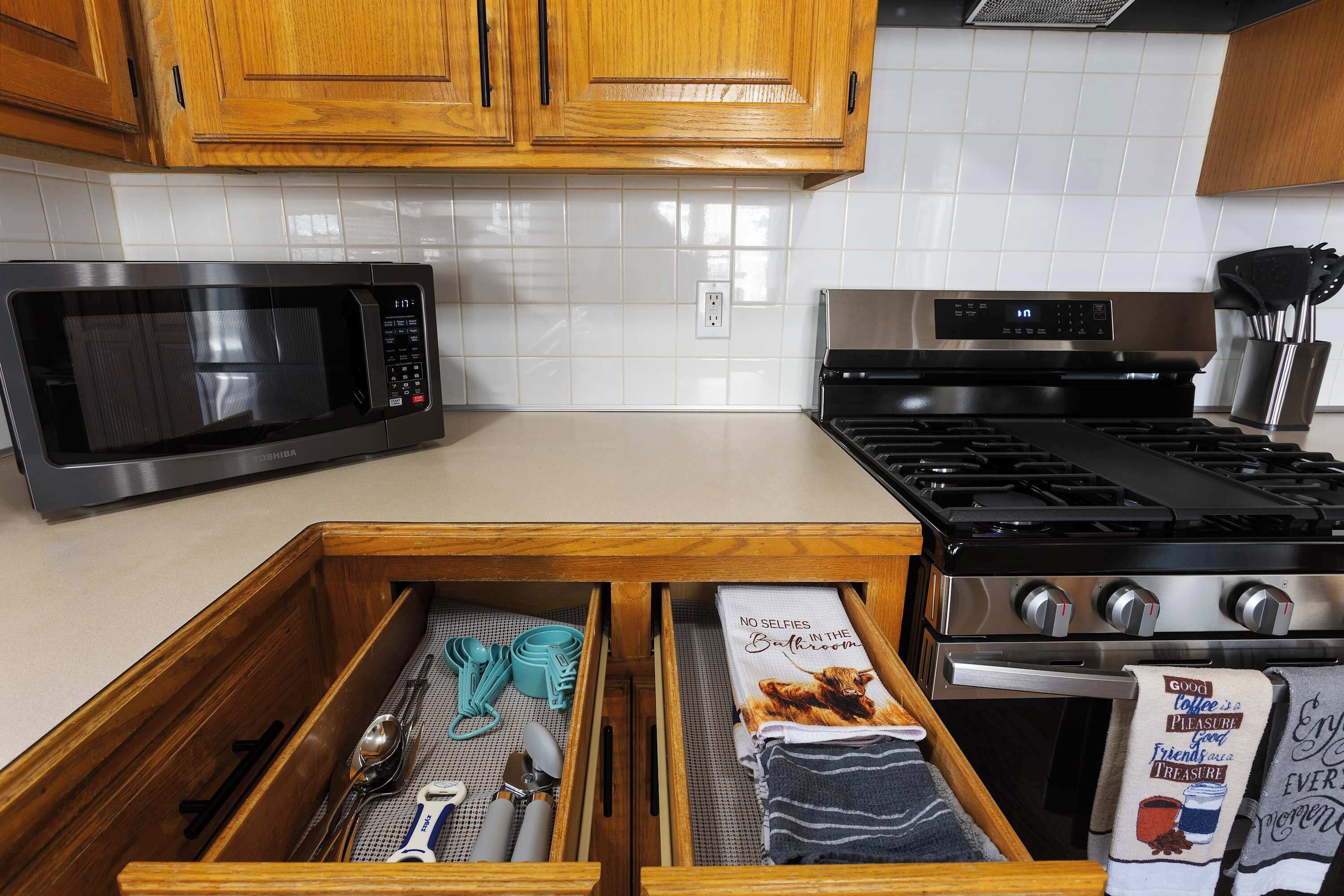 Une cuisine avec des meubles de rangement en bois, un four à micro-ondes, une cuisinière et un organiseur de tiroir contenant des ustensiles.