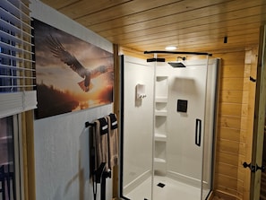 A shower with a glass door, wooden ceiling, and a towel rack with towels.