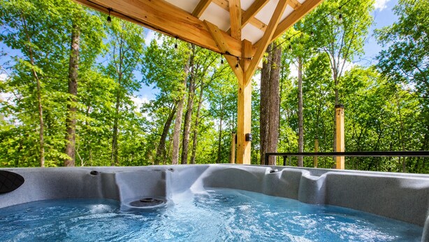 A hot tub in a covered outdoor area with a wooden roof and surrounded by trees.