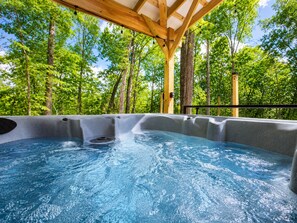 Un jacuzzi en un área exterior cubierta con techo de madera rodeado de árboles.
