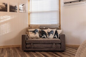 A cozy living room with a gray sofa, three decorative pillows, and a window with blinds.