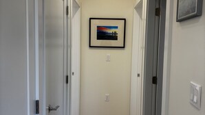 A hallway with wooden flooring, white walls, and doors on either side. There is a framed picture on the wall. - New 2BR Garden Suite with AC and private patio (Burnaby)