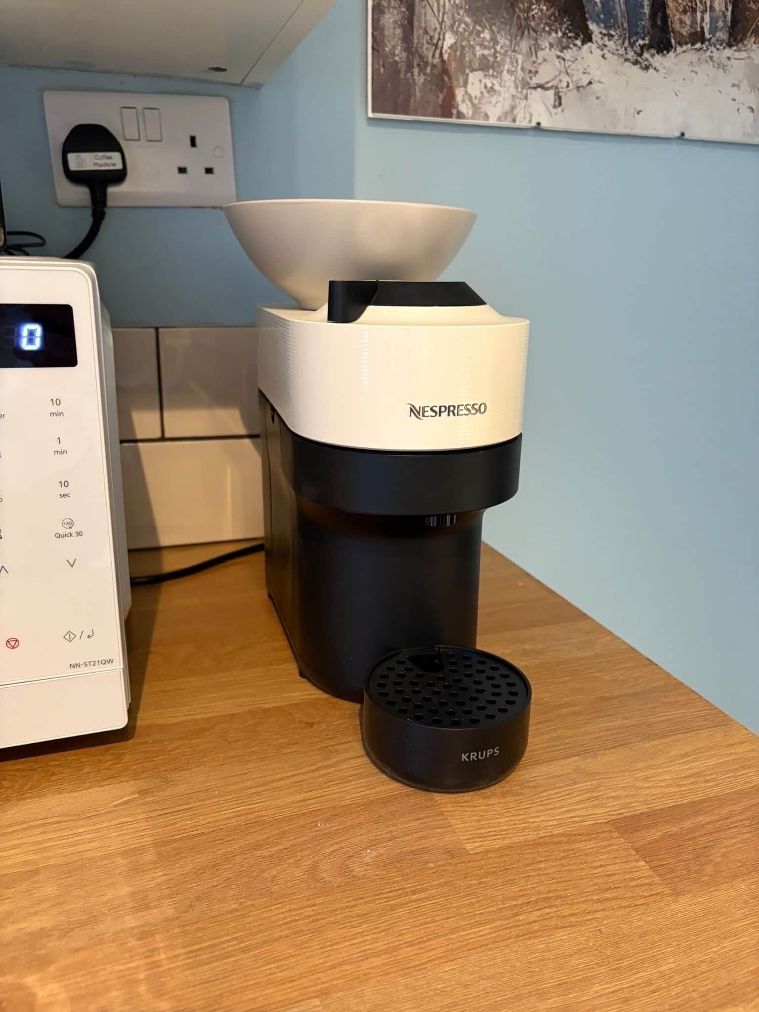 Uma máquina de café Nespresso sobre uma bancada de madeira, com um moedor de café Krups ao lado.