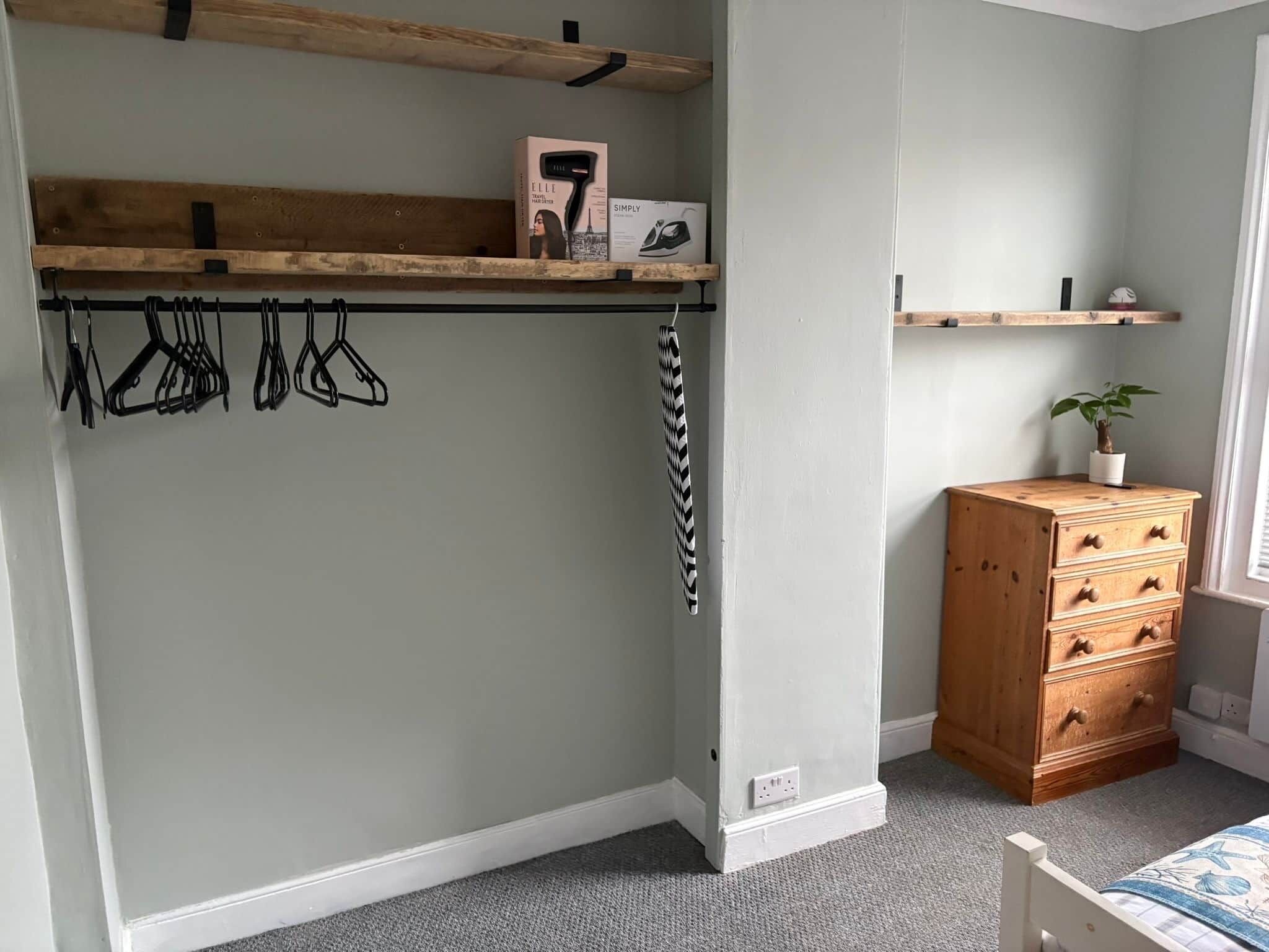 A bedroom with a built-in wardrobe, a wooden dresser, and a hanging coat rack.