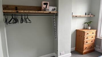 A bedroom with a built-in wardrobe, a wooden dresser, and a hanging coat rack.
