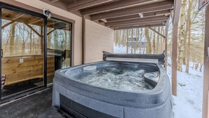 Een hottub onder een houten pergola met een glazen deur die leidt naar een houten kamer.