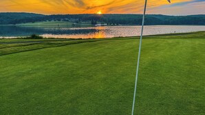Een golfbaan met vlaggenstok, waterpartij en een zonsondergang.