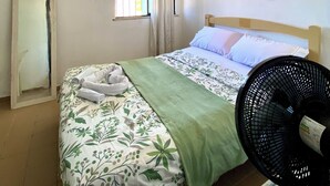 A bedroom with a bed, a mirror, a window with curtains, a fan, and a door. - Greenhouse Cumbuco, a cozy house 3 minutes from the village. (Caucaia)