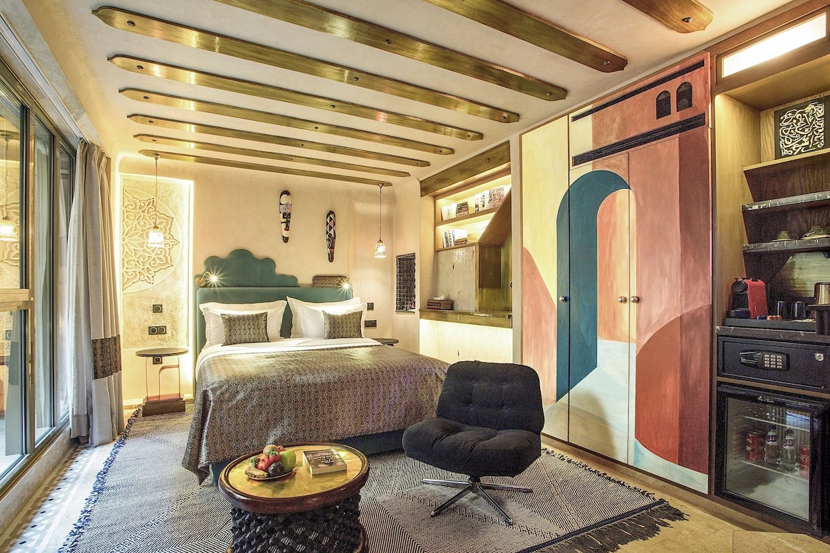 Una habitación de hotel moderna con una cama grande, una zona de estar con una silla, una mesita y un armario de diseño único.
