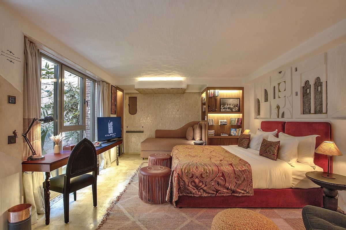 Un dormitorio amplio con una cama grande, un escritorio con silla, un televisor y una ventana con cortinas.
