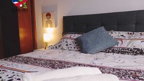 Una habitación de hotel con una cama cubierta por una colcha estampada, una almohada gris y dos toallas blancas.