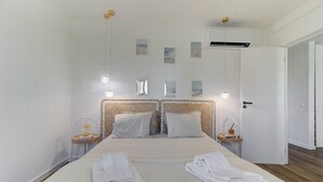 A hotel room with a large bed, two bedside tables, a wall-mounted air conditioner, and a door to another room. - Refúgio no Mar, Armação de Pêra (Silves)