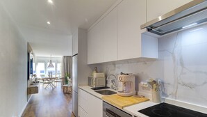 A modern kitchen with white cabinets, a built-in oven, and a dishwasher. There is a dining area with a table and chairs visible in the background. - Refúgio no Mar, Armação de Pêra (Silves)