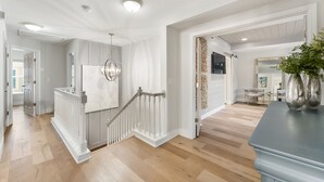 A spacious hallway with a wooden floor, a white staircase, and a modern light fixture. -  Art Inspired Coastal Retreat in Ponte Vedra Near Beach Ideal for Families (Nocatee)