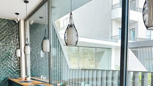 Uma área de bar moderna com um balcão de madeira comprido, banquetas de metal preto e luminárias pendentes.