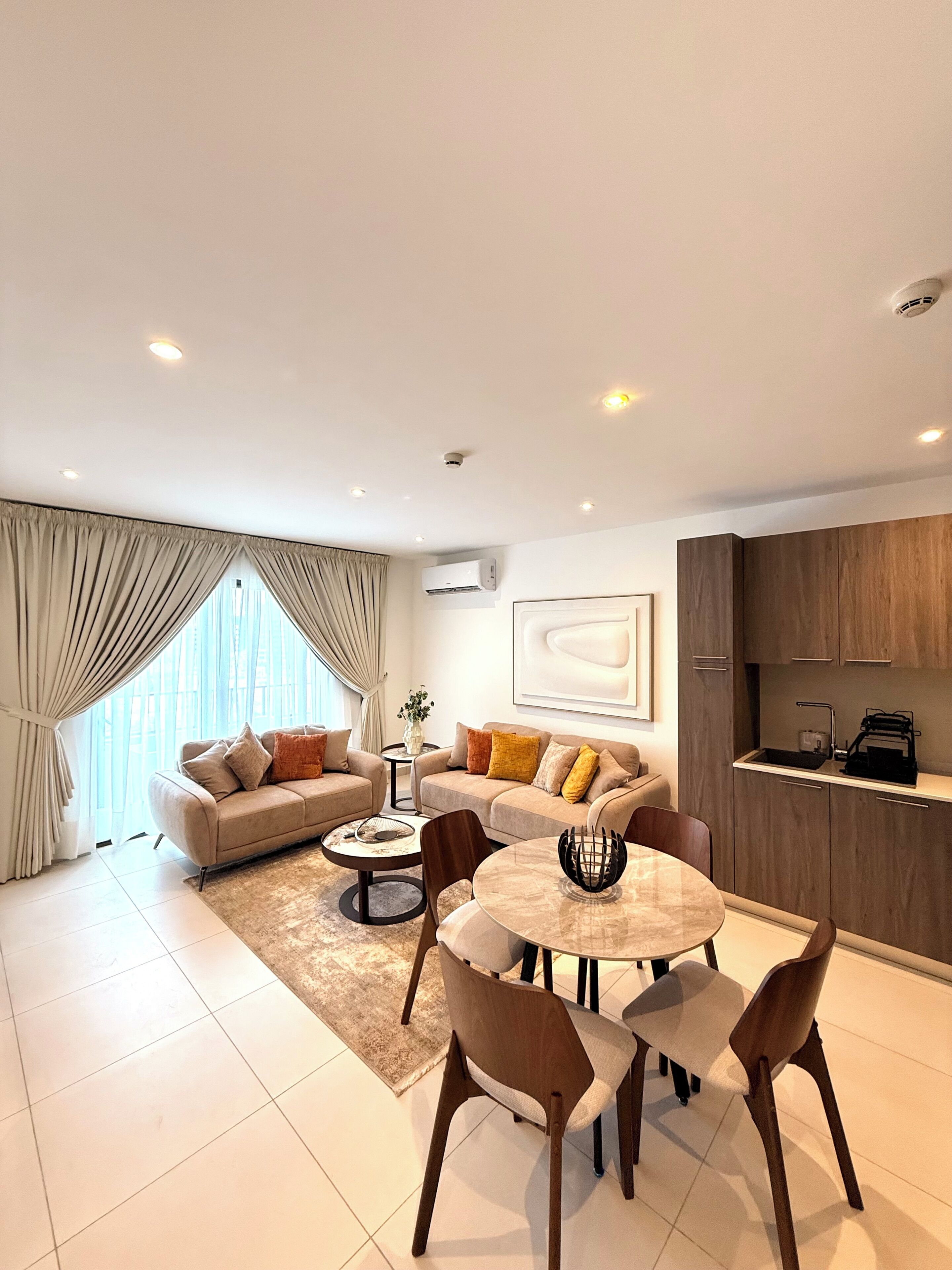 A modern living room with a dining area, a sofa set, a coffee table, and a kitchen area with wooden cabinets.