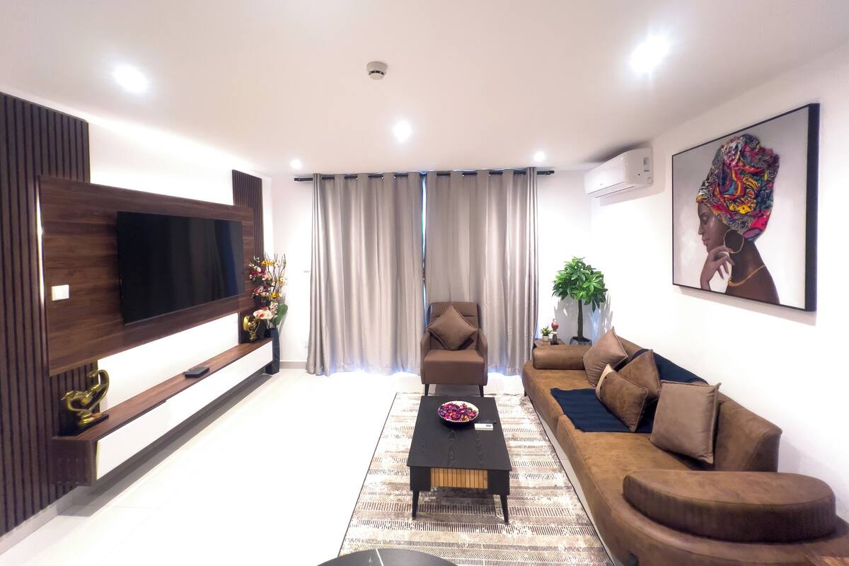 Un salon moderne avec un téléviseur à écran plat, un canapé marron, une table basse et un tapis à motifs.