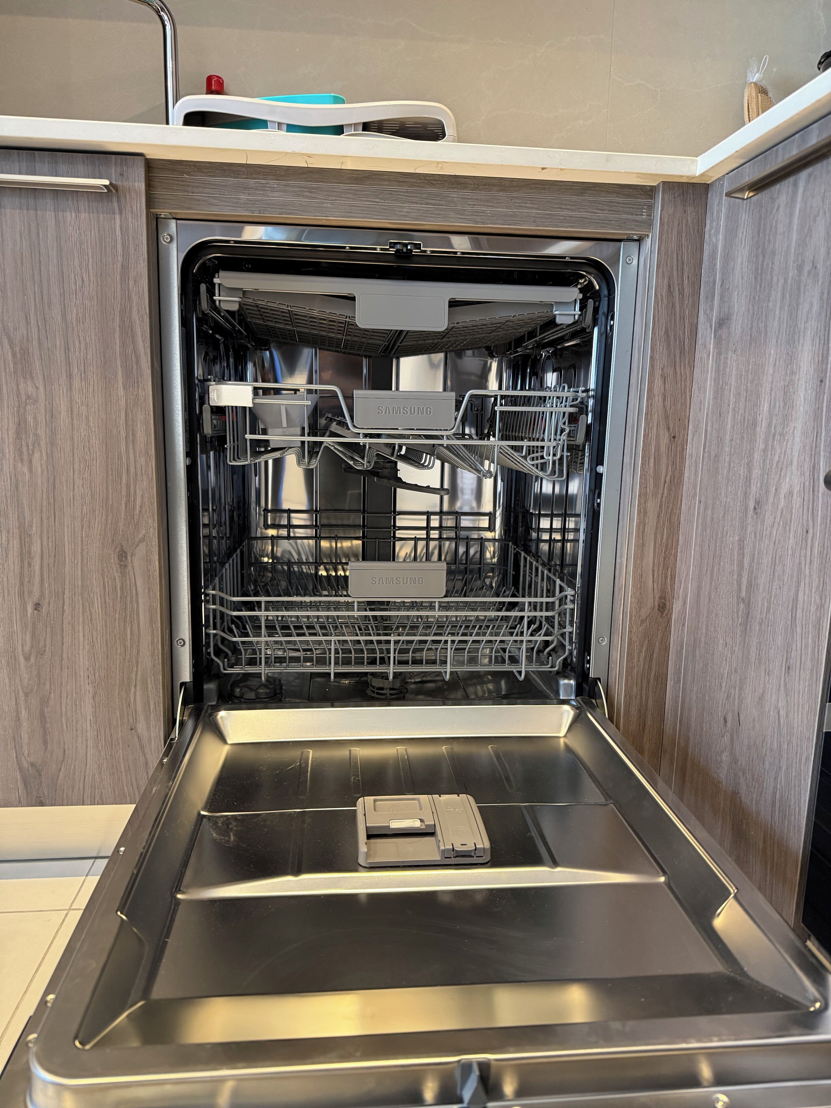 An open dishwasher with a stainless steel interior and a Samsung label.