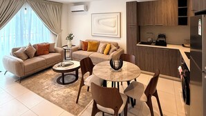 Uma sala de estar moderna com um sofá, uma mesa de jantar e cadeiras. Há uma cozinha com armários e uma geladeira.