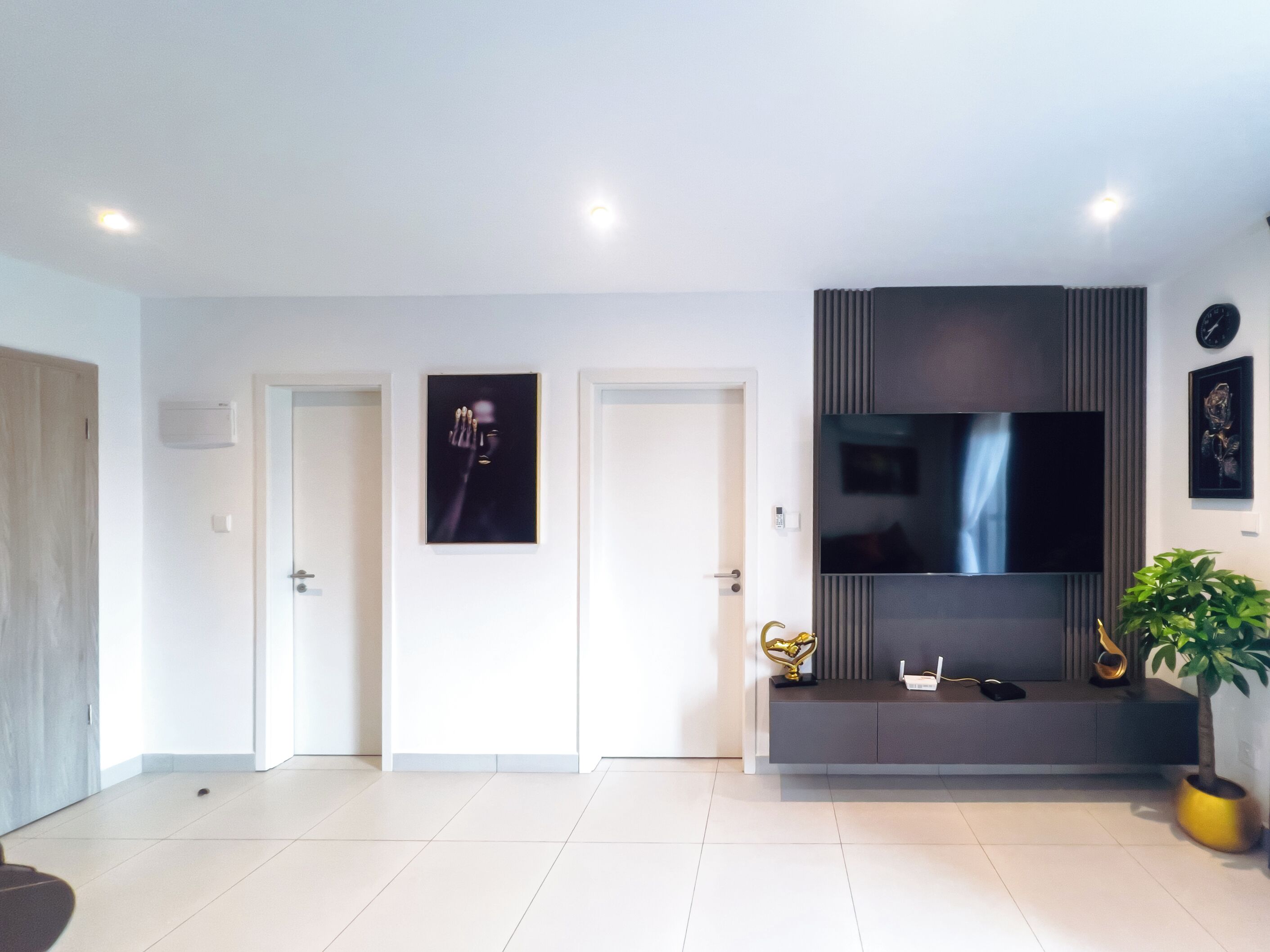 Una sala de estar moderna con un televisor de pantalla plana, una planta y un objeto decorativo sobre una mesa consola.