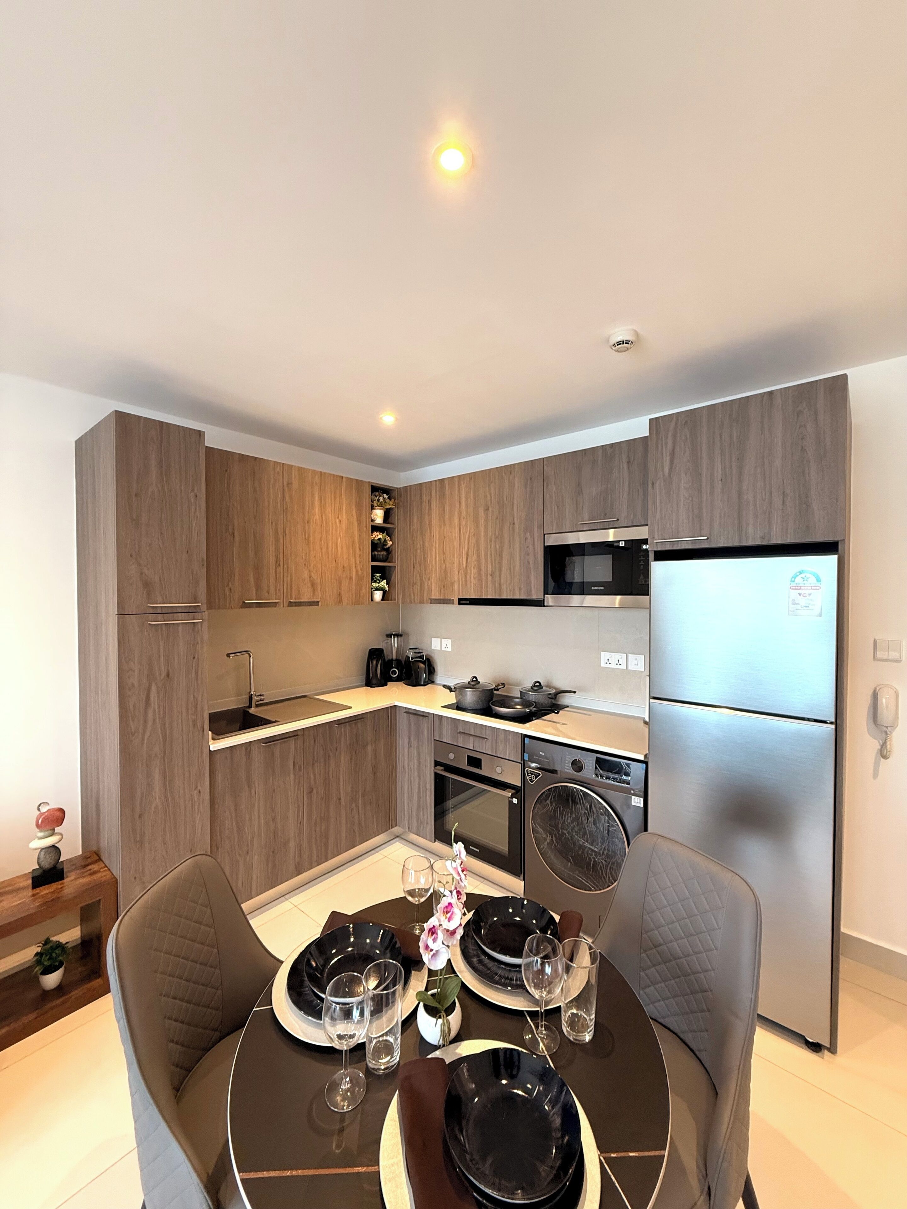 A modern kitchen with wooden cabinets, a stainless steel refrigerator, and a dining area with a round table and chairs.