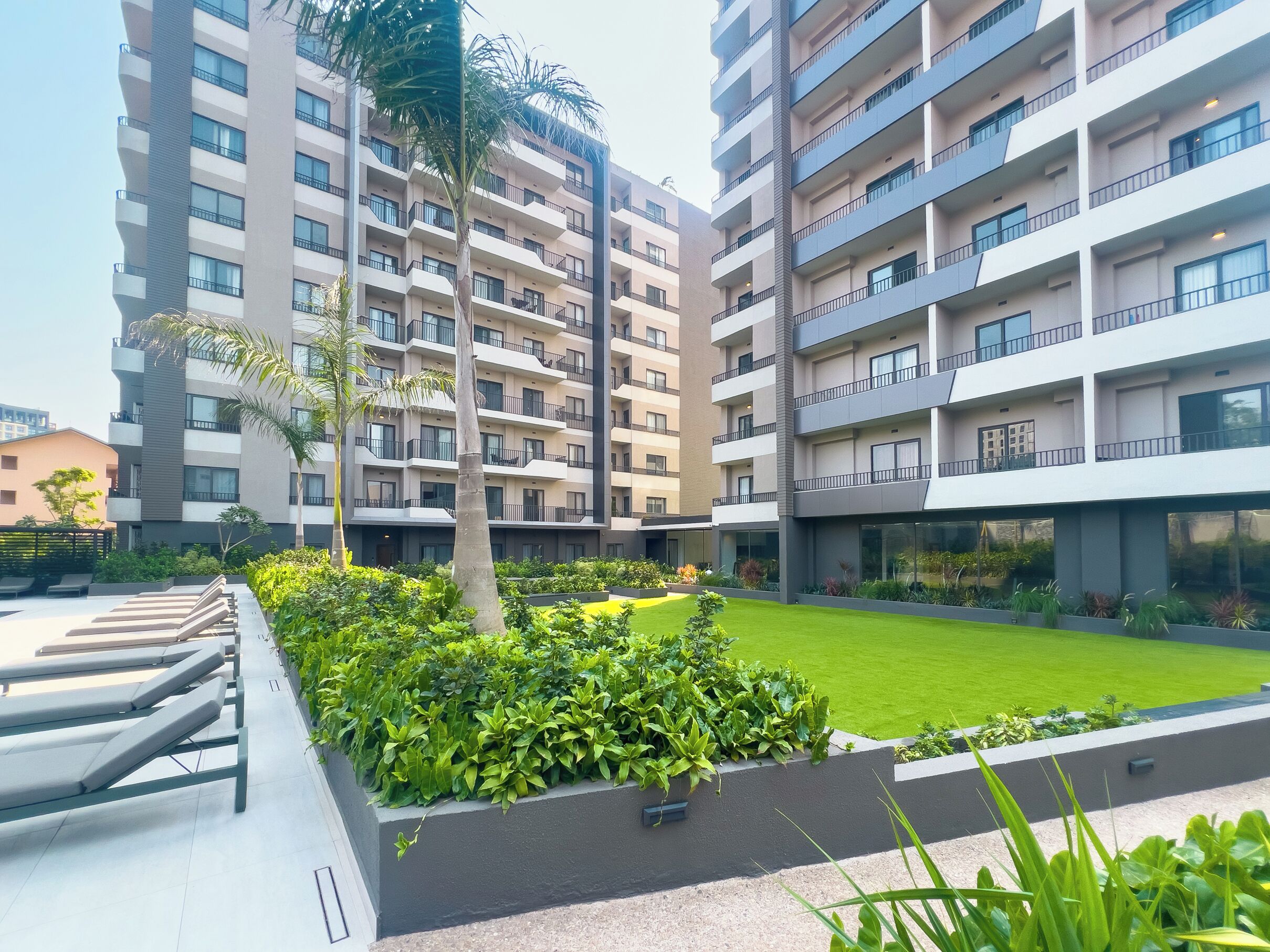 A modern apartment complex with multiple balconies, a well-maintained lawn, and outdoor seating areas.